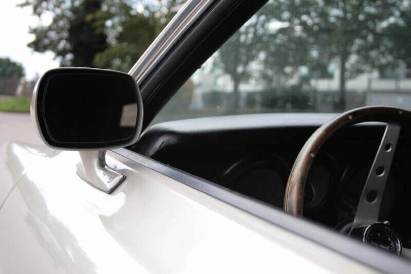 Blik langs de zijspiegel naar het stuur in de cockpit van de Ford Mustang; de auto die je zelf mag besturen.