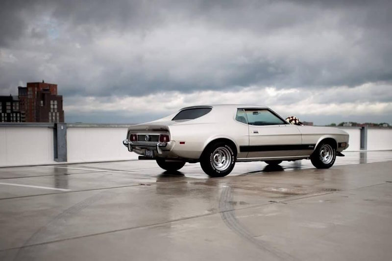 De Ford Mustang ingezet als stoere trouwauto langs de waterkant, sfeervol vastgelegd tijdens regenachtig weer op een bruiloft.