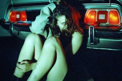 Een model poserend tegen de achterzijde van de zilveren Ford Mustang Grande voor een fashion shoot van het kledingmerk Blouson Noir.