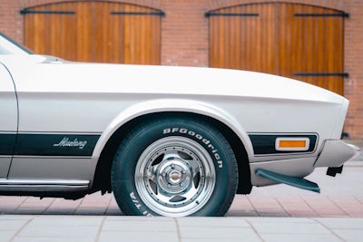 Gedetailleerde close-up van de gepoetste chromen velg en de zilveren wielkast van de Ford Mustang Grande, symbool voor de kwaliteit van de restauratie en de luxe uitstraling.